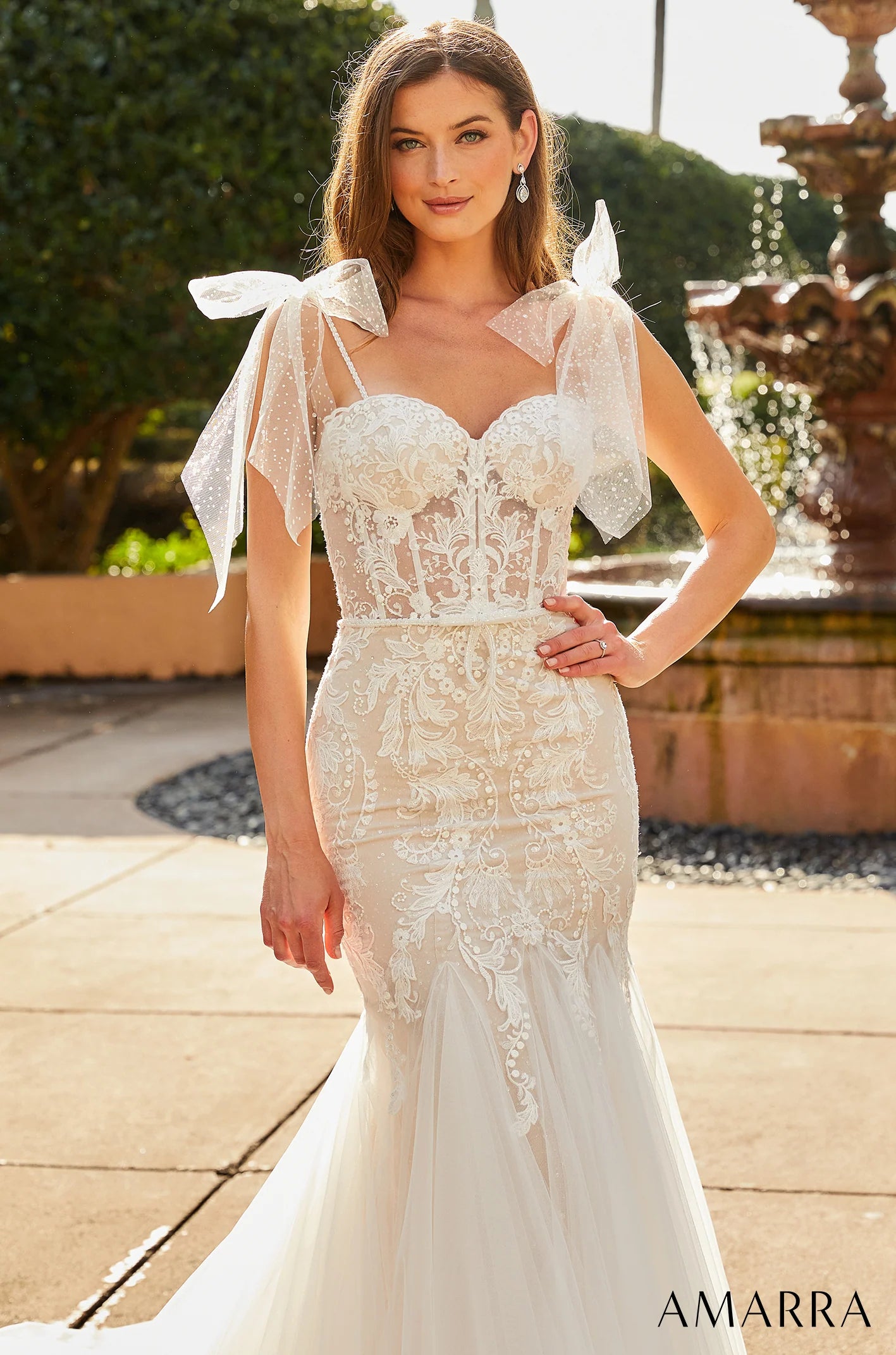 Woman wearing a white lace wedding dress with sheer sleeves in an outdoor setting.