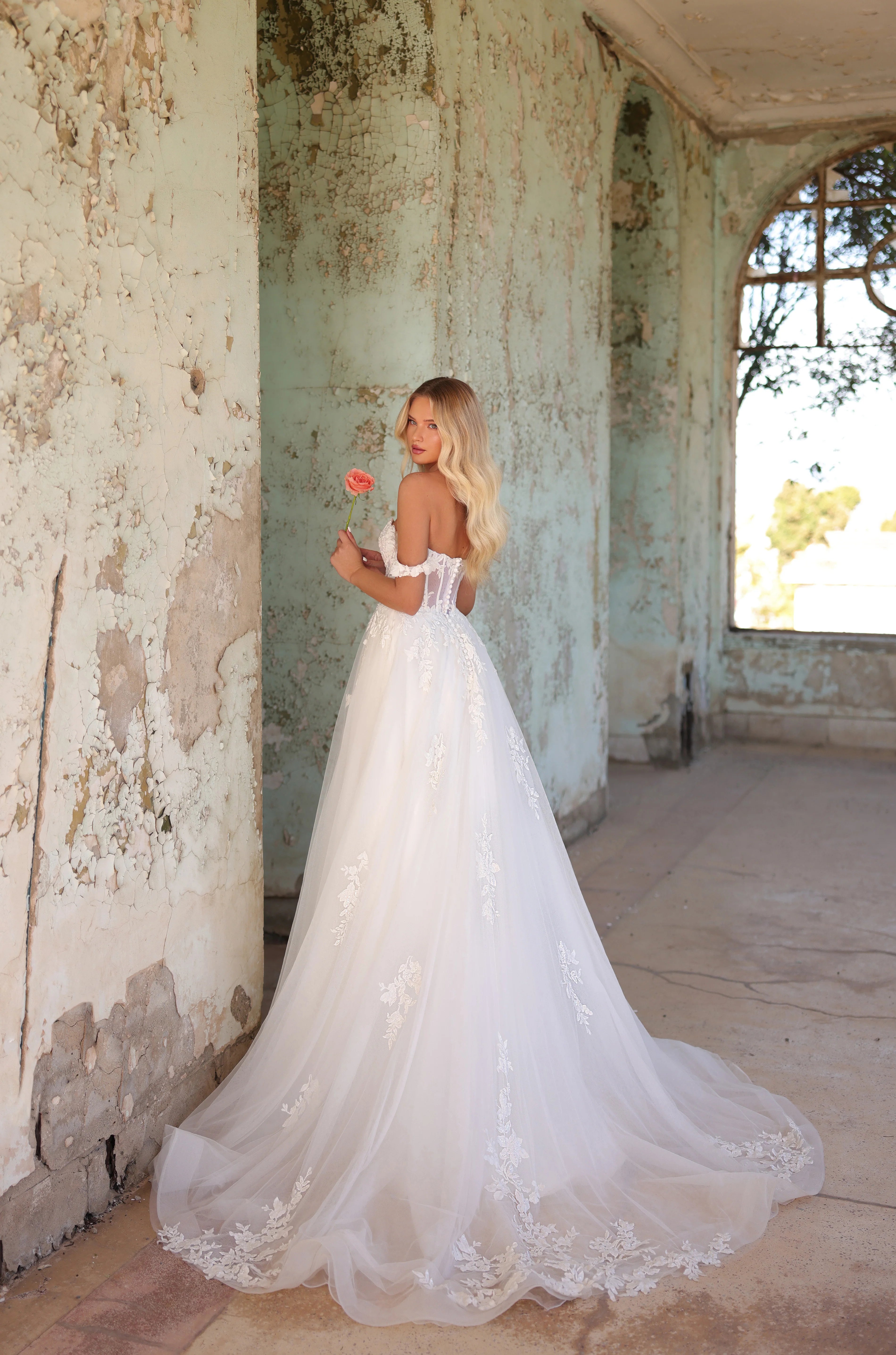 Woman in a white wedding dress holding a red flower in an old, dilapidated building.